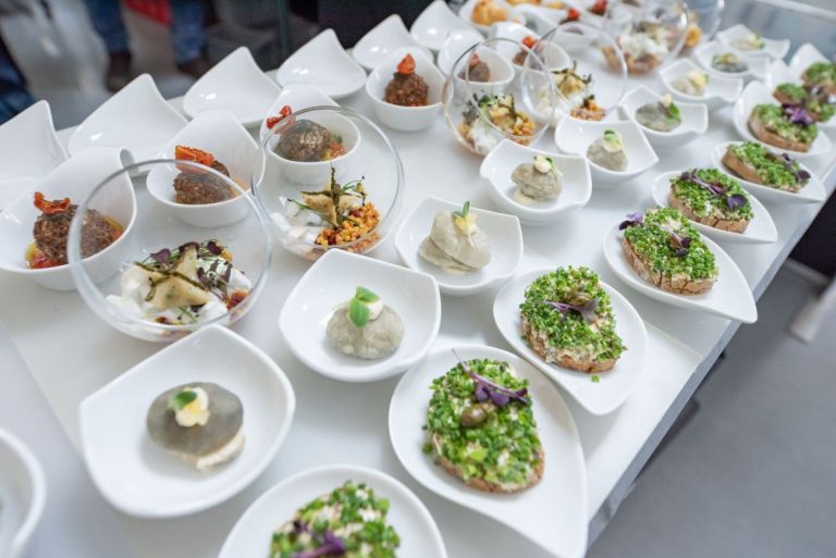 Vorspeisenbuffet: Ein Tisch mit einer großen Auswahl an kunstvoll angerichteten Vorspeisen in weißen Schälchen, darunter belegte Brote, kleine Kugeln und Salate.
